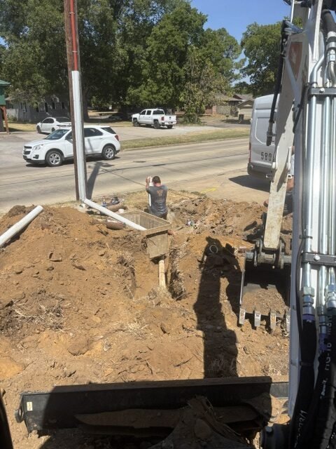Titan Plumbing crew member working on an excavated sewer line beside an excavator